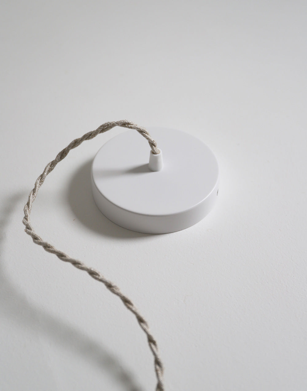 Suspension dôme arrondi blanche avec cordon torsadé beige posé sur une surface claire.
